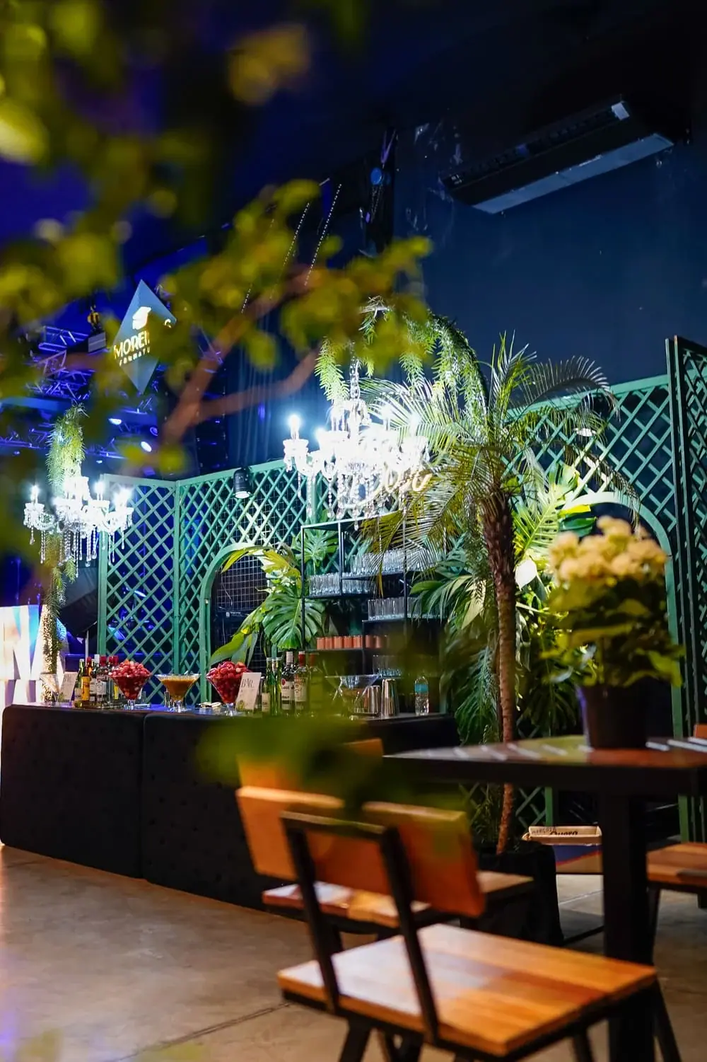 Bar temático decorado com plantas, treliça e iluminação ambiente.