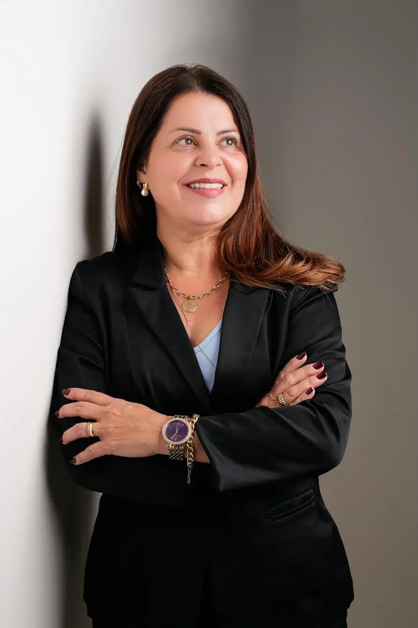 Valéria Moreira de blazer preto e braços cruzados, olhando para o lado.